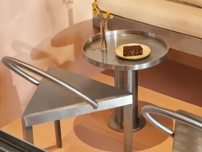 Cozy living space with a couch, chair, dining table, and small round table with a plate, surrounded by vases and featuring wood and metal materials