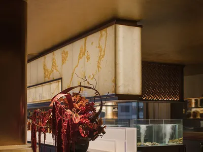 A well-lit interior design showroom with a large vase filled with flowers on a table in front of a gold-adorned wall, surrounded by smaller vases and decorative elements