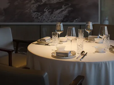 A luxurious dining area with a large table set for a meal, surrounded by chairs, wine glasses, and fine china