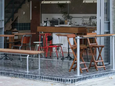 Modern restaurant interior with dim lighting, white walls, and wooden flooring, featuring a dining area with tables and chairs and a kitchen area