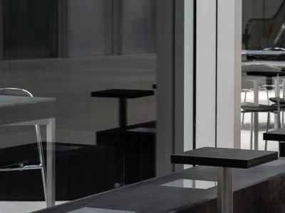 A modern restaurant seating area with multiple wood tables and metal chairs arranged in rows, with a neutral color palette and subtle lighting
