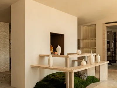 A minimalist interior design showroom featuring a table with six vases of various sizes and shapes, set against a clean white wall