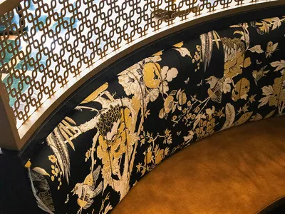 Ornate bench with floral design in a living area, possibly a dining room, with a black frame and Asian-inspired aesthetic