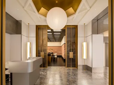 Elegant hotel lobby with marble flooring, gold accents, and high ceilings, featuring a large open space with a dining area and lounge