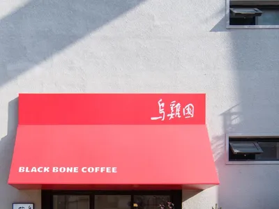 現代咖啡店，紅色遮陽篷、大片窗前有樹木、盆栽植物，以及乾淨現代的白色灰色調室內