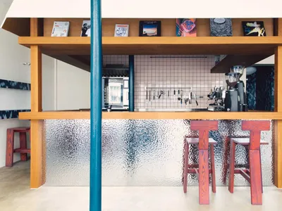 Cozy modern kitchen with wooden floors, walls, and a counter with stools and a coffee maker, surrounded by scattered books