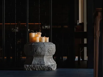 A calm and inviting dining space with a black and white color scheme, featuring a stone pedestal with lit candles, two chairs, and a dining table