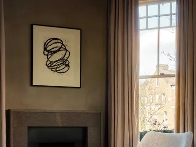 Cozy living space with a white chair in front of a fireplace, two windows on either side, and natural light from the windows