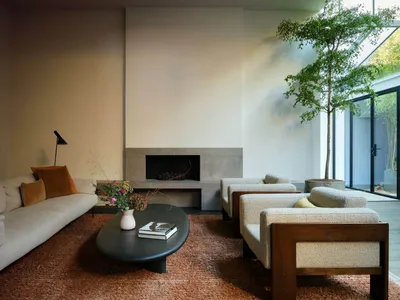 Cozy living room with a fireplace, two couches, chairs, a potted plant, and a book, set against a backdrop of a large window and natural light