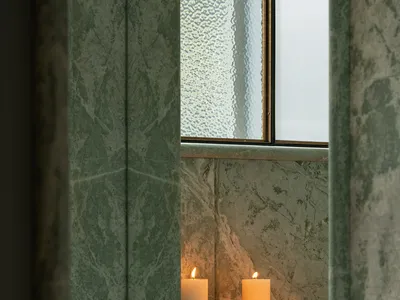 Bathroom scene with a marble wall featuring three lit candles, creating a warm and relaxing ambiance