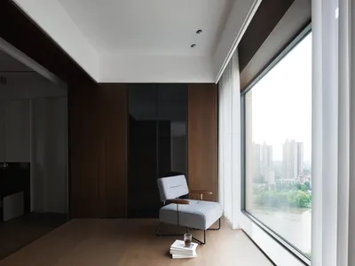 Cozy living space with a wooden chair in front of a large window, surrounded by books and natural light