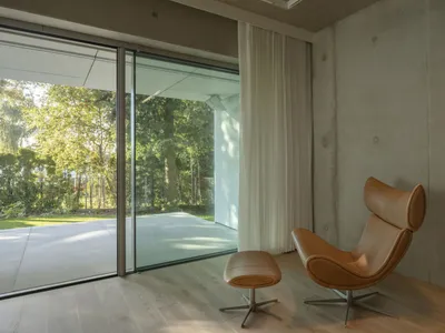 Open living area with a leather chair near a window, a couch against the wall, and a second chair in the room, with a modern and minimalist feel and neutral tones