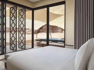 A hotel bedroom with a white-covered bed, two chairs, and a dining table, creating a calm and inviting atmosphere