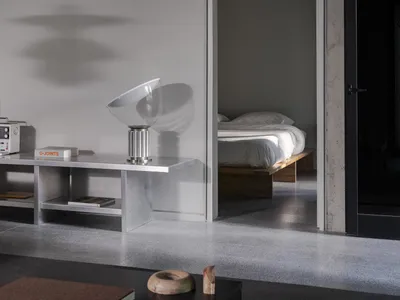 Modern minimalist bedroom with concrete walls and floors, featuring two beds, a chair, and a dining table in a clean and organized space