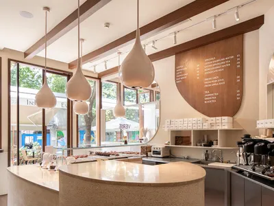 A modern restaurant interior with a counter featuring cups, bottles, and donuts, surrounded by chalkboard signs and a dining table in the background
