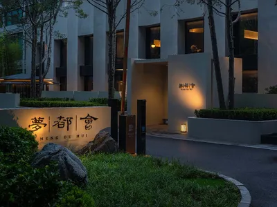 A hotel entrance with a stone wall, rock garden, and trees surrounding the area, creating an elegant and inviting ambiance