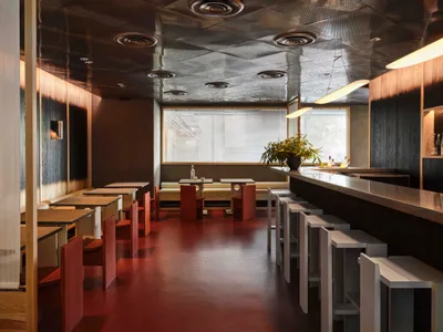 A modern restaurant or bar with a long counter and stools, dining tables, and red tile flooring