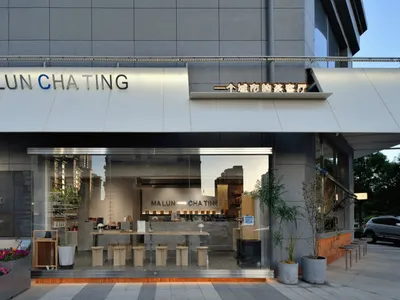 A modern Asian restaurant with grey walls, natural light, and comfortable seating areas with potted plants