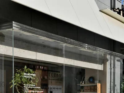 A welcoming retail space with a glass front, featuring potted plants, bottles, and chairs, creating a comfortable shopping environment