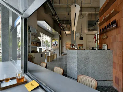 A cozy retail space with a wooden counter and shelves, displaying bottles and books, with advertisements and signs on the walls, and multiple chairs for patrons