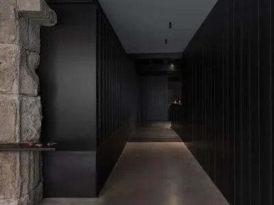 A narrow dark hallway with a wooden door at one end, lit by two wall lights