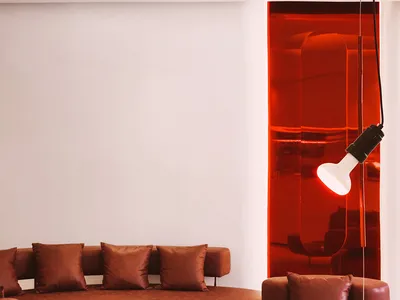 A modern living area with brown leather chairs and couches arranged around a coffee table, surrounded by red walls and white accents