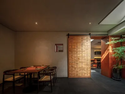 A warm and inviting restaurant dining area with wooden furniture, multiple dining tables, and a large wooden door leading to another room