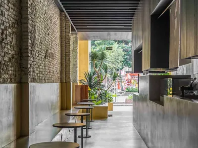 Empty modern restaurant interior with cement walls and floor, featuring tables and chairs in a clean and minimalistic setting