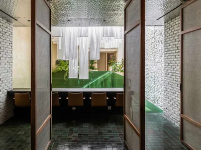 A modern Asian restaurant with tables, chairs, potted plants, and hanging white fabric, well-lit for a welcoming atmosphere