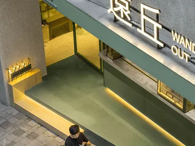 A modern Asian restaurant with green walls and a glass door, featuring a relaxed and inviting atmosphere with two people enjoying drinks outside