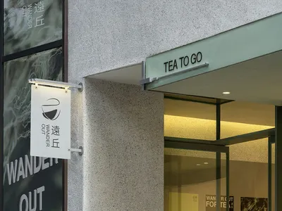 溫馨咖啡廳，白色牆面、灰石元素與玻璃門，門口招牌寫著「Wander Out For Tea」