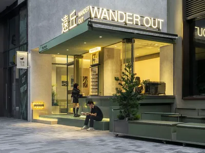 Modern Asian restaurant with green walls, glass front, and outdoor seating area with potted plants and a chair