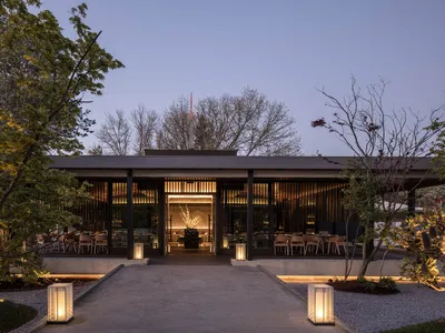 Modern restaurant with a black facade, multiple tables, chairs, and potted plants, emphasizing functionality and comfort