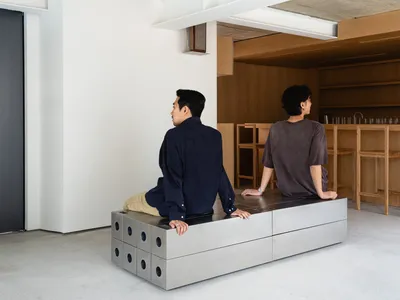 A relaxed office-living space with a dining table, cups, and a book, featuring a comfortable atmosphere and two people engaged in conversation
