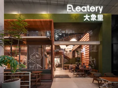 Modern Asian restaurant with a green facade, wooden elements, and a mix of colored walls, featuring a large dining area with tables and chairs and potted plants