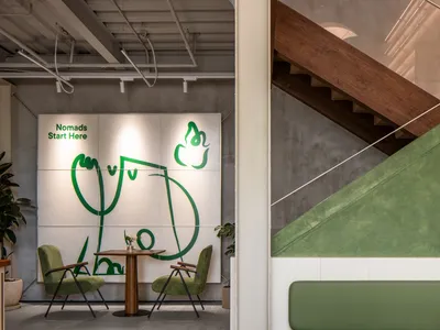 Industrial restaurant interior with green walls, wooden stairs, and dining tables with chairs, a potted plant adding greenery to the space