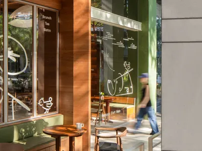 Cozy Asian restaurant with a wooden exterior, green accents, and large windows, featuring dining tables, chairs, umbrellas, and potted plants