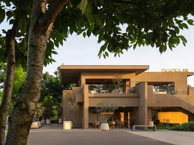 A brown building with a yellow accent and a large staircase leading to a second floor, surrounded by chairs in a gathering or event space