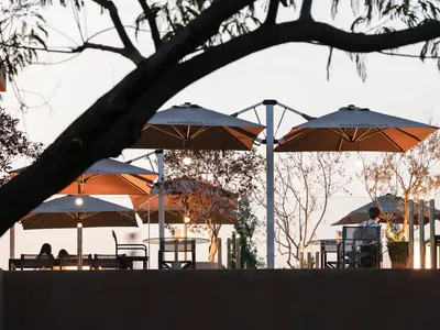 An outdoor dining area at night with multiple tables and chairs under umbrellas, creating a cozy and inviting atmosphere for guests to relax and socialize