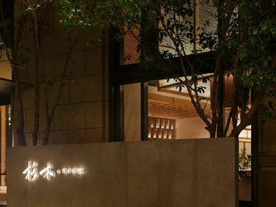 A well-lit Asian restaurant with a stone exterior and wooden interior, surrounded by potted plants and large windows