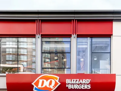 紅色屋頂現代餐廳的外觀，擁有眾多窗戶和大大的「DQ Blizzard Burgers」招牌，側邊有兩個時鐘