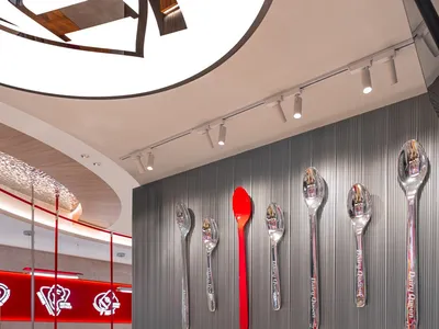 A modern restaurant dining area with white tablecloths, chairs, and decorative spoons mounted on the walls, creating a clean and inviting atmosphere
