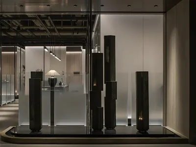 Elegant showroom with a glass wall displaying various sculptures and vases, featuring stone and organic shapes, in a sophisticated atmosphere