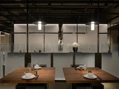 Sophisticated restaurant interior with wooden tables, glass partitions, and modern design elements, featuring wine glasses and cups on two dining tables