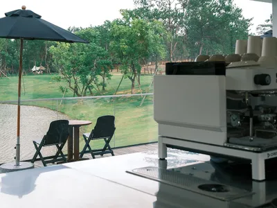 A patio dining area with a table and chairs, shaded by an umbrella, surrounded by a serene forest setting
