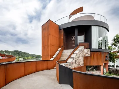 A modern orange building with a unique design near a lake, featuring a large staircase and artistic architecture