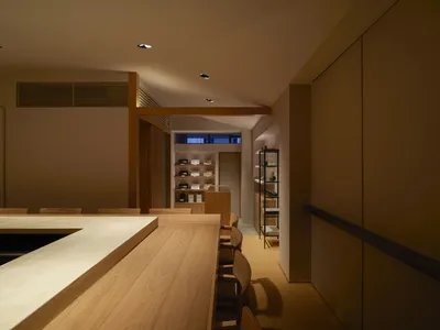 A well-lit dining space with a long wooden table surrounded by chairs, bottles, and a warm ambiance