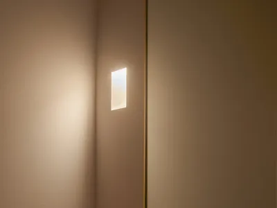 A clean bathroom with a sink on the right, a mirror above it, and two lights, one near the left edge and one near the center, creating a well-lit and inviting atmosphere
