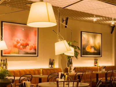 Dimly lit restaurant interior with a bar counter and chairs, surrounded by dining tables and bottles