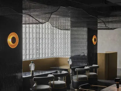 Modern restaurant interior with black and gold decorations, tables, chairs, and couches in a spacious dining area